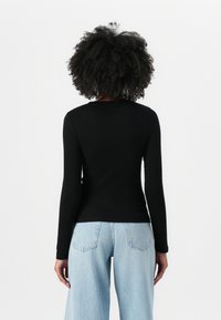 Svart, langermet tettsittende topp, med ribbet tekstur og rund hals, sammen med lyseblå vide jeans. Enkelt design, uten synlige mønstre eller detaljer.