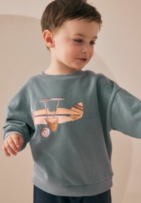 Light blue sweatshirt featuring a colorful airplane graphic, round neckline, and ribbed cuffs. Soft texture, casual design for children.
