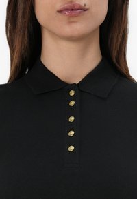 Zwart polo shirt met een textuurafwerking, voorzien van een kraag en zes gouden knopen langs de knoopsluiting. Eenvoudig en klassiek ontwerp.