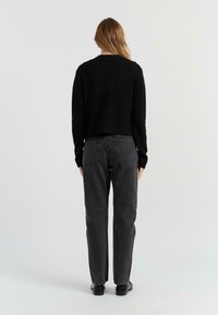 Maglione nero in maglia con design cropped, abbinato a jeans grigi scuri a vita alta. Entrambi presentano una texture liscia e uno stile minimalista.