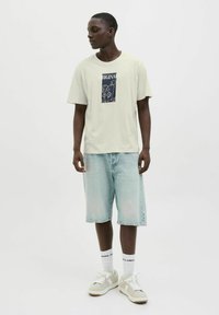 Lichtgroen katoenen t-shirt met een marineblauwe grafische print, gecombineerd met lichtblauwe denim shorts en crèmekleurige sneakers. Effen witte sokken met merklogo.