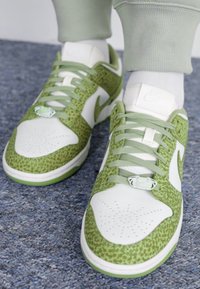 Zöld és fehér tornacipő leopárdmintázattal, textúrált anyaggal, perforált orral és zöld fűzőkkel. Nike logó látható.