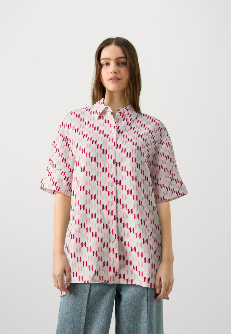Cămașă cu buton în material ușor, cu un model geometric în nuanțe de roz și roșu. Mâneci scurte și croială lejeră, cu detalii la guler.