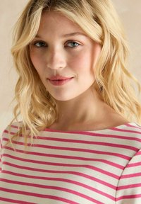 Paski top z dekoltem w łódkę, z naprzemiennymi różowymi i białymi paskami. Materiał wydaje się miękki i lekki.