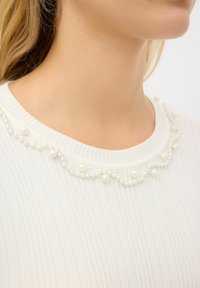 Weißer gerippter Pullover mit einem runden Ausschnitt, der mit einer gewellten Reihe kleiner dekorativer Perlen verziert ist, um dem Detail mehr Charme zu verleihen.