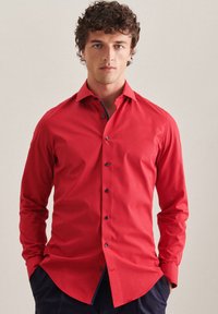 Chemise rouge à manches longues en tissu lisse avec une coupe ajustée. Dotée de boutons sombres et de détails contrastants au col et aux poignets.