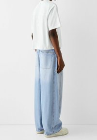 Pohodlné bílá bavlněná tričko v volném střihu doplněné o světle modré oversized džíny. Tenisky s gumovou podrážkou, znatelné švy na džínách.