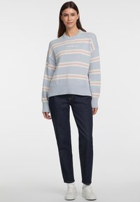 Hellblau gestreifter Pullover mit pinken und weißen Linien, gerippte Bündchen und Saum, kombiniert mit dunkelblauen Jeans und weißen Sneakern.