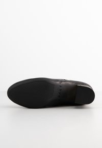 Botín negro de cuero hasta el tobillo con suela de goma texturizada, cremallera lateral y logo de DKNY en el talón. Acabado suave y diseño elegante.