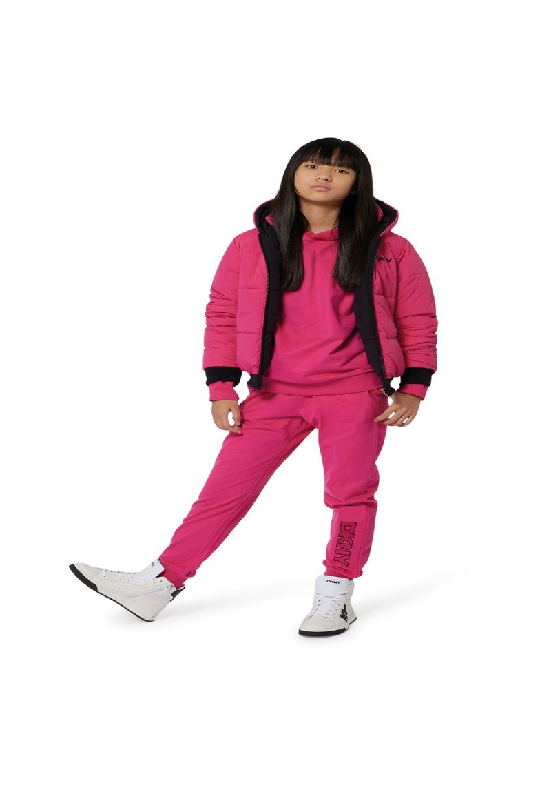 Chaqueta acolchada rosa con detalles negros, sudadera rosa y pantalones de chándal a juego. Zapatillas deportivas altas blancas. Presenta el logo "DKNY" en los pantalones.