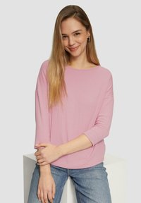 Lichtroze geribbelde top met een ronde halslijn en driekwart mouwen, gecombineerd met blauwe jeans. De stof voelt zacht en glad aan.