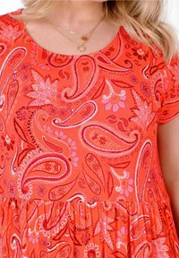 Czerwona sukienka w wzór paisley z krótkimi rękawami, okrągłym dekoltem i marszczonym pasem. Zawiera kwiatowe akcenty w kolorze różowym i białym.