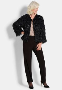 Zwarte nepbont jas met paillettenaccenten, ronde halslijn en brede mouwen, gecombineerd met zwarte broeken en hoge hakken.