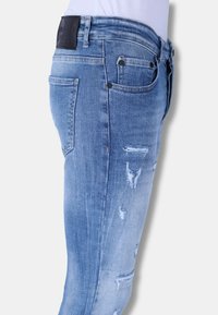 Lichtblauwe denim jeans met een slim fit, voorzien van versleten details en een leren patch op de tailleband. Standaard five-pocket ontwerp.