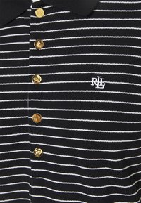 Černobílé pruhované polo tričko s límečkem, se zlatými knoflíky a vyšitým logem bílé barvy na levé části hrudi.