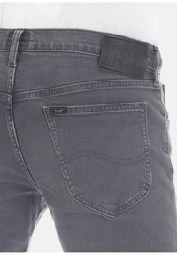 Jeans de mezclilla gris oscuro con un bolsillo trasero y una etiqueta de cuero negro en relieve. Presenta costuras sutiles y un diseño de corte clásico.