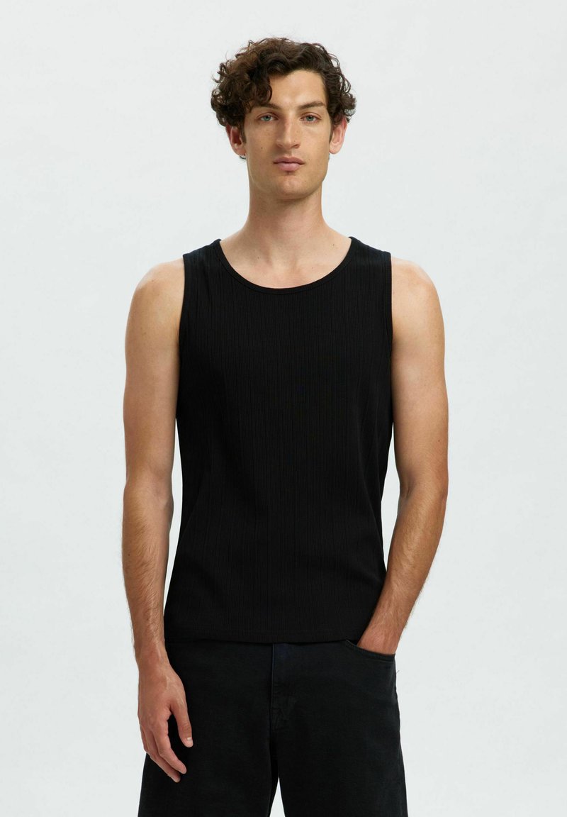 Débardeur noir sans manches avec une texture côtelée, encolure ronde et design ajusté. Porté avec un pantalon sombre, avec une poche sur le côté.