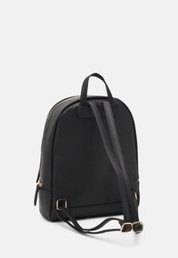 Sac à dos noir au design arrondi, fabriqué en tissu durable, doté de quincaillerie dorée, de deux sangles et d'une poignée supérieure.