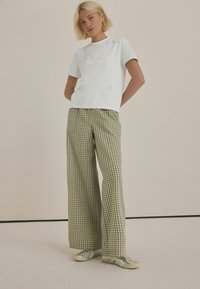 Chemise blanche à manches courtes avec des embellissements floraux, associée à un pantalon large en vichy vert et des baskets argentées. Tenue moderne simple et décontractée.
