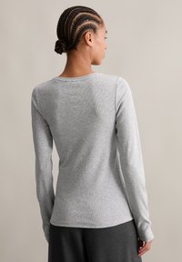 Hosszú ujjú, világosszürke ing, puha, bordázott anyagból készült. Klasszikus kerek nyakkivágással és feszes szabással rendelkezik.