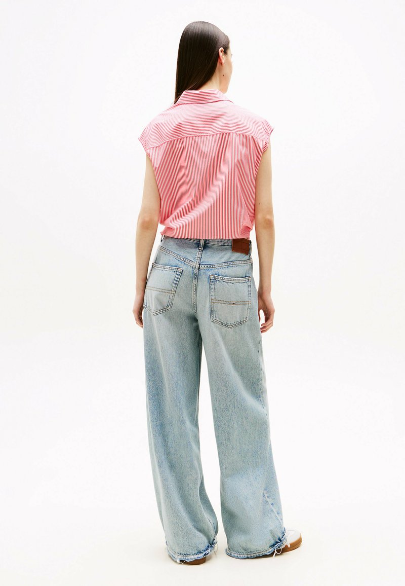 Chemise à rayures rouges et blanches à manches courtes associée à un jean large bleu clair. Le jean a une taille haute et des poches arrière avec une étiquette en cuir.