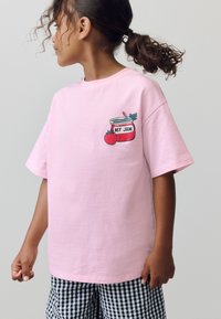 Rosa bomullst-shirt med tryckt syltburk, en jordgubbe och texten "MY JAM" på vänstra bröstområdet. Korta ärmar, avslappnad passform.