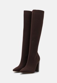 Bottes en tissu côtelé marron jusqu'au genou avec un bout pointu et un talon bloc, présentant une texture lisse et un design ajusté.