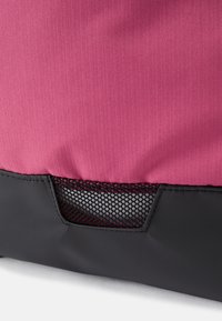 Saco de tecido rosa com uma superfície texturizada, apresentando um bolso de malha preta na parte inferior e uma base lisa preta.