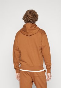 Felpa marrone con una vestibilità relax, dotata di un cappuccio ampio, polsini e orlo a costine, realizzata in tessuto morbido. Nessuna grafica o motivo visibile.