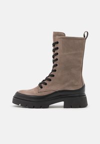 Lace-up enkelboot in taupe suede met een zwarte rubberen zool. Kenmerkt zich door een chunky platform, gestikte accenten en een lusje aan de bovenkant.