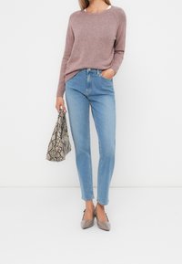 Rosa Strickpullover, hellblaue Jeans mit hoher Taille, graue spitze Ballerinas und eine Tasche mit Schlangenmuster. Glatte Textur und legere Silhouette.