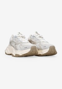 Zapatillas deportivas de color beige claro con una parte superior de malla texturizada, detalles en crema, suelas gruesas y franjas en contraste en la lengüeta.