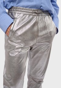 Metalické stříbrné joggery s elastickým pasem a šňůrkou. Obsahují dvě boční kapsy a hladkou, lesklou texturu.
