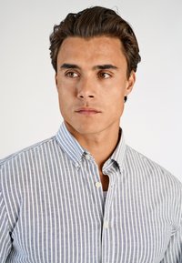 Πουκάμισο με κουμπιά, σε ανοιχτό μπλε και λευκή ριγέ μοτίβο. Κατασκευασμένο από βαμβάκι, διαθέτει κλασικό γιακά και λεπτομέρειες με κουμπιά.