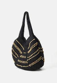 Μαύρη πλεκτή τσάντα με υφή, διακοσμημένη με χρυσές χάντρες διατεταγμένες σε κυματοειδή μοτίβο και δύο στιβαρές λαβές για μεταφορά.