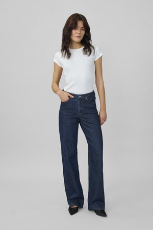 White fitted t-shirt with short sleeves, paired with dark blue wide-leg jeans. The jeans feature a front button and pockets. Black pointed shoes.