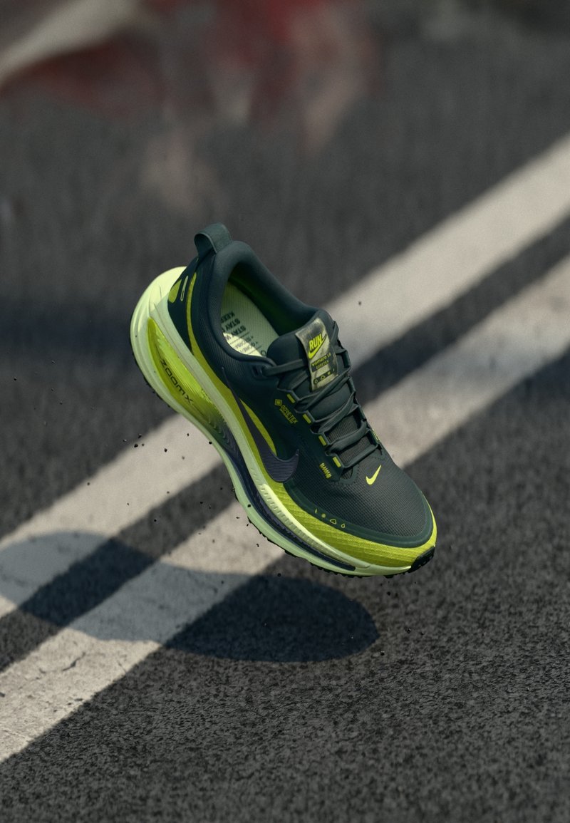 Chaussure de course noire et jaune fluo flottant au-dessus d'une route asphaltée avec des marquages blancs des voies.