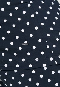 Marinblått tyg med kontrasterande vita prickar, med en liten metall-logotag och synliga sömnadsdetaljer.