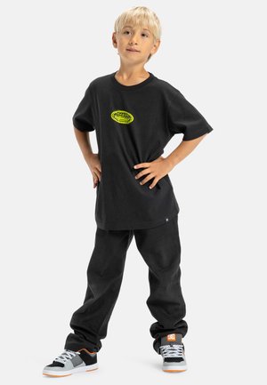 Zwarte katoenen t-shirt met een ronde hals en een oversized pasvorm, met een neongele logo. Gepaard met zwarte loszittende pants en sneakers.