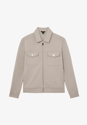 Világosszürke dzseki puha anyagból, elöl cipzárral, hegyes gallérral és két mellkasi zsebfedővel, patentgombokkal.