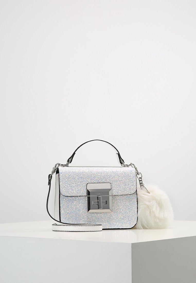 Sac à main argenté scintillant avec un fermoir métallique, des accents noirs et un charm en fausse fourrure blanche amovible. Comprend une poignée supérieure et une bandoulière ajustable.