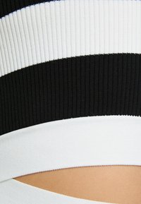 Närbild av svart och vit ribbad stickad tyg med horisontella ränder och ett diagonalt utskärning som visar huden under.