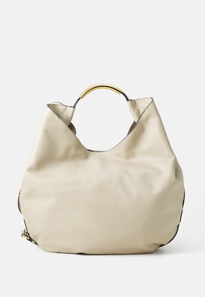 Beige leather handbag with slouchy shape and rounded gold accent handle, set against a white background.