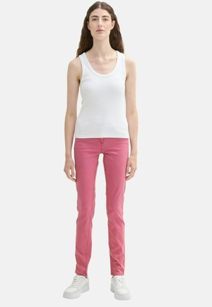 Un débardeur blanc côtelé associé à un jean rose slim et des baskets blanches. La tenue présente un design simple et des couleurs unies sans motifs.