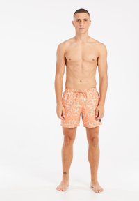 Zwemshorts in oranje met een bloemenpatroon, voorzien van een elastische tailleband en koord. Glad materiaal. Model staat blote voeten, op een neutrale achtergrond.