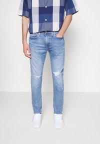 Ljust blå rivna jeans med slim fit, kombinerat med en kortärmad skjorta i blått och grått rutmönster samt vita sneakers.