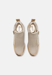 Scarpe slip-on beige con tomaia in maglia, dettagli metallici dorati, punta rotonda e pannello laterale elastico. Logo stampato di lato.