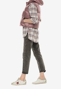 Růžová péřová vesta s kapucí nošená přes kostkovanou flanelovou košili. V kombinaci se šedými džíny a bílými teniskami s červenou hvězdou.