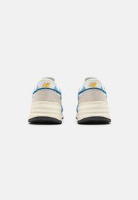 Vista posteriore di scarpe da atletica caratterizzate da una combinazione di suede grigio chiaro e mesh blu, con un sottopiede crema e una suola in gomma nera. Logo giallo.