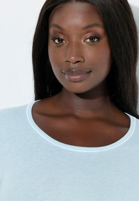 Lyseblå stof top med rund halsudskæring, med en kontrasterende hvid kant. Glat tekstur og tætsiddende pasform.